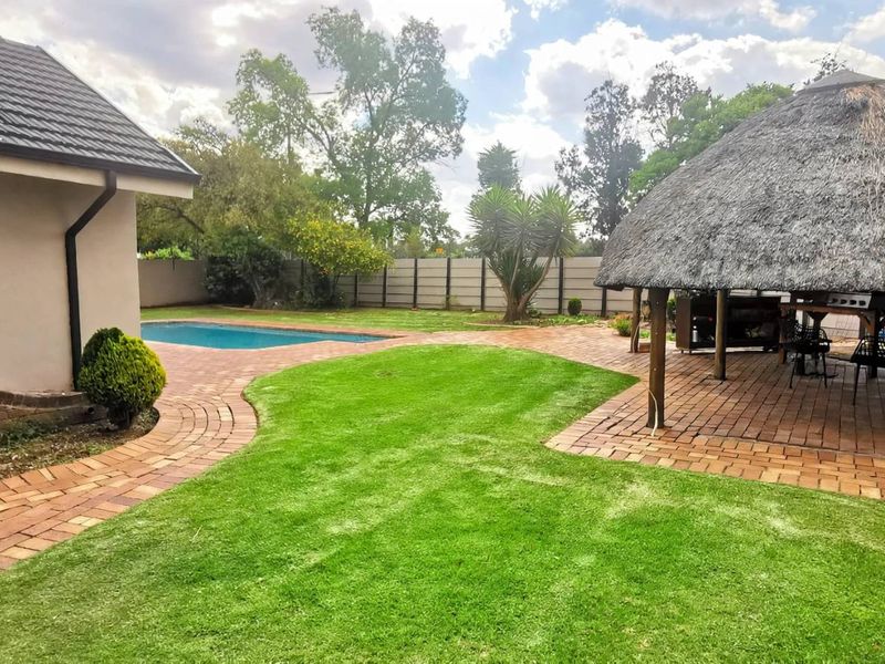 Rear garden featuring a swimming pool, brick paved pathways, and a traditional thatch lapa entertainment area.