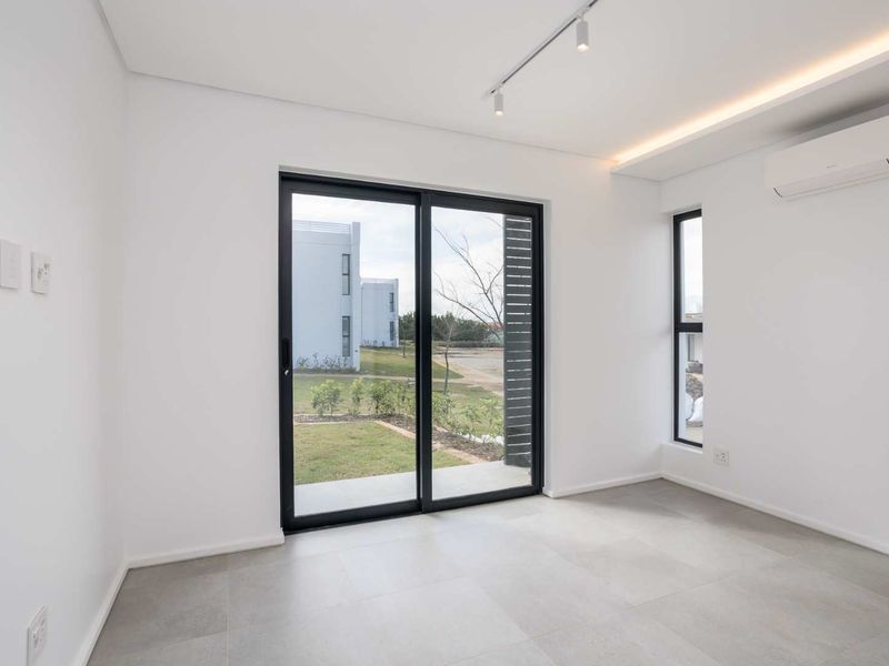A bright, modern, and empty bedroom featuring tiled floors, a split-system air conditioner, and a sliding glass door leading to an outdoor area.