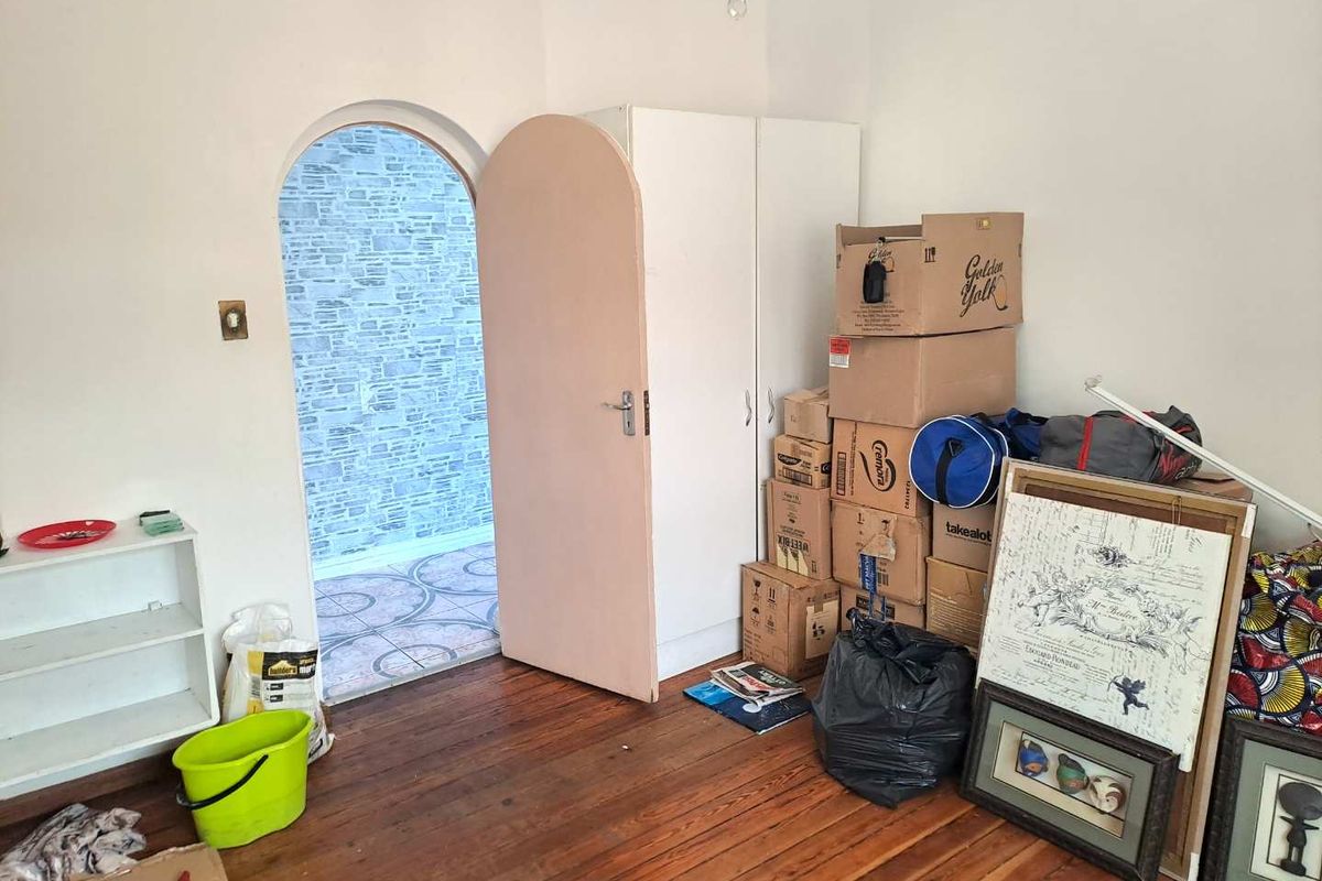 A bedroom featuring original timber flooring, a built-in wardrobe, and an arched doorway leading to an adjacent tiled space.