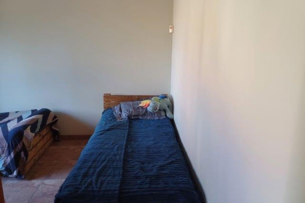 A simple bedroom featuring tiled flooring and neutral wall finishes, providing a functional space for rest.