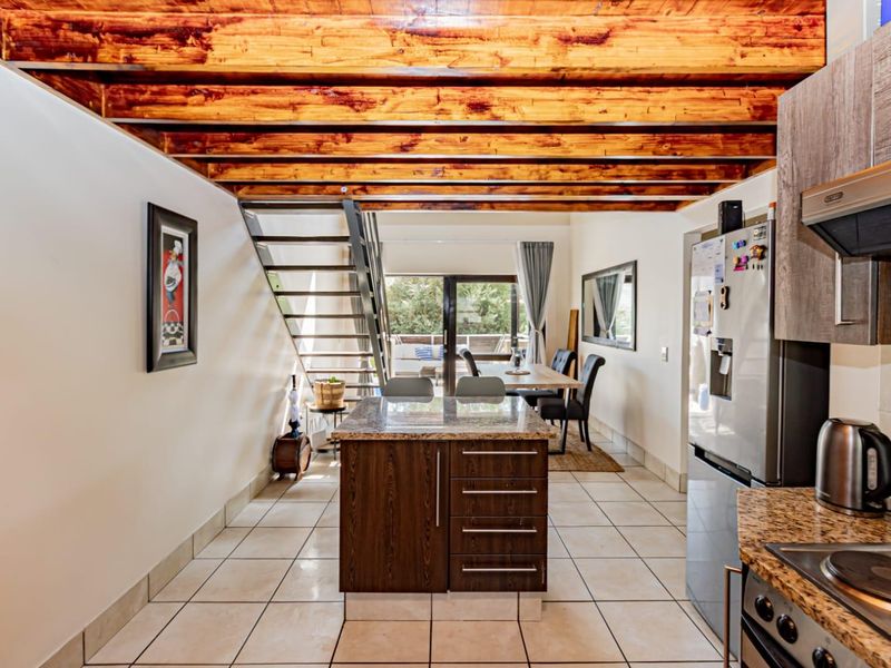 Open-plan living area featuring a kitchen with granite countertops, exposed timber ceiling beams, and a staircase leading to an upper level.