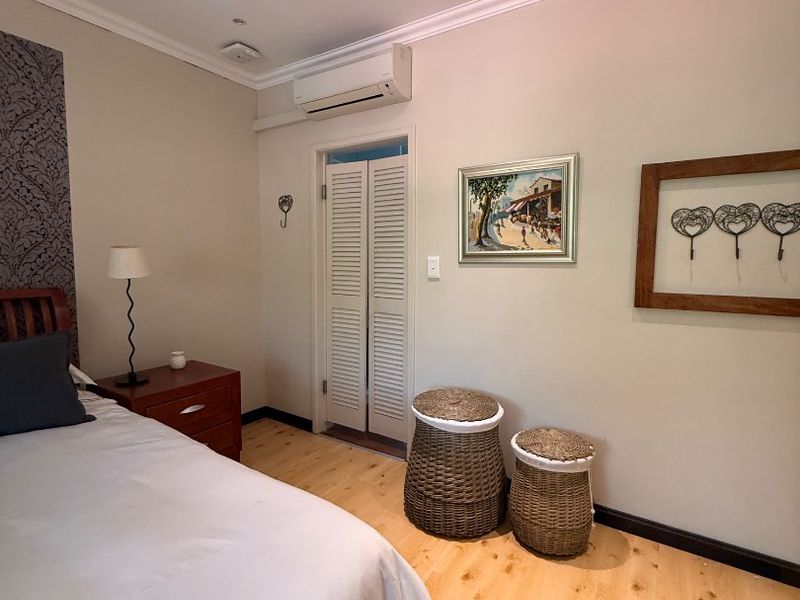 A well-maintained bedroom featuring light laminate flooring, cove molding, recessed lighting, and a wall-mounted split-system air conditioning unit.