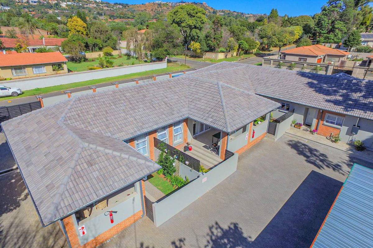 Aerial view of a townhouse complex featuring tiled roofing, brick exterior walls, and a paved driveway area with a private patio.