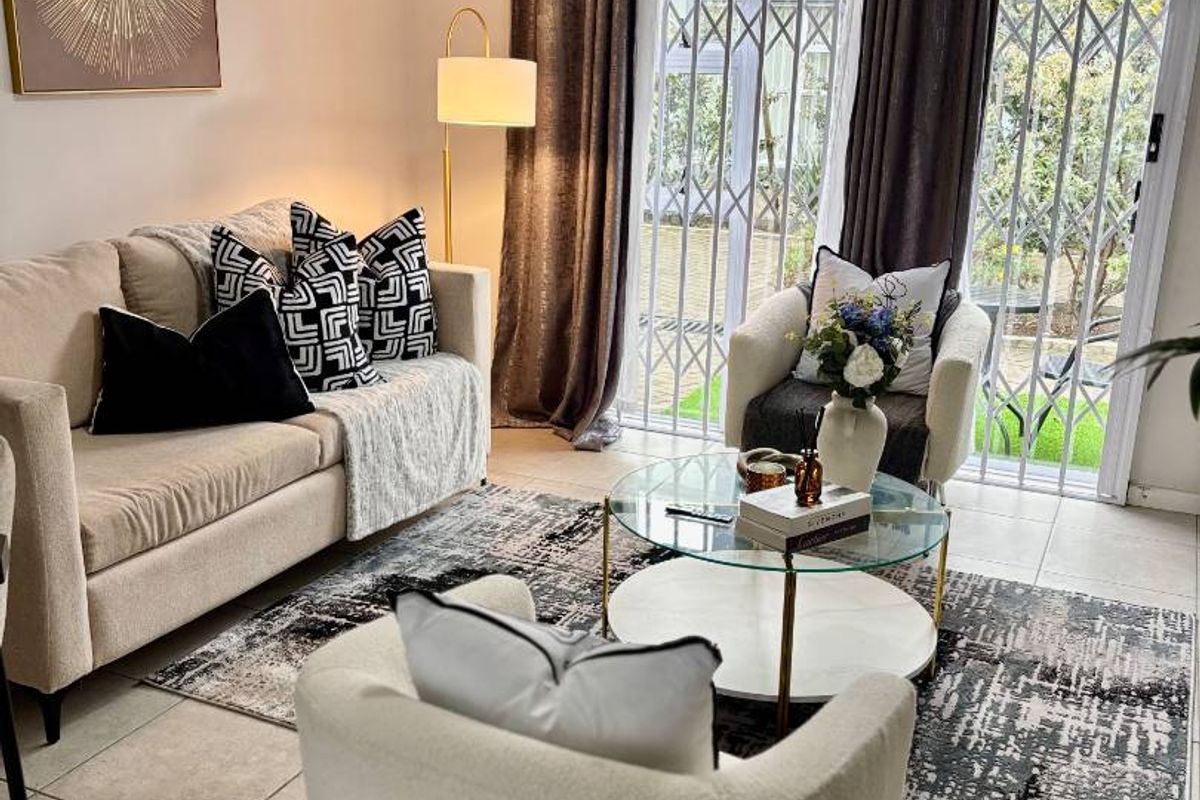 A well-lit living room featuring neutral tiled flooring and a sliding glass door with an integrated security gate leading to the outdoors.