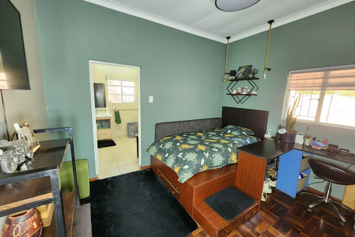 A bedroom featuring parquet flooring, a built-in desk, and an en-suite bathroom access, finished with green walls and cove cornicing.