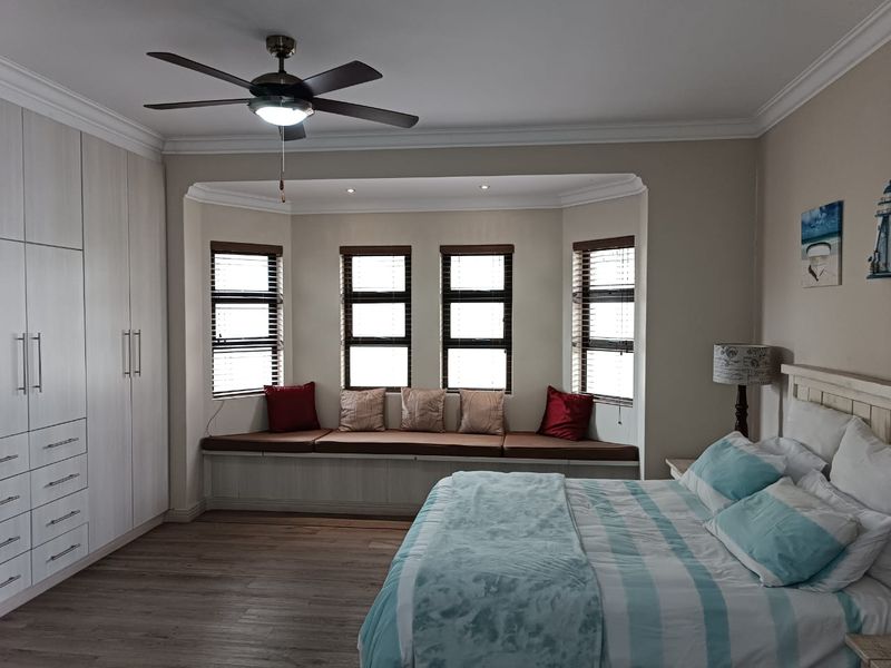 A well-maintained bedroom featuring built-in cupboards, laminate flooring, and a charming bay window with a built-in window seat.