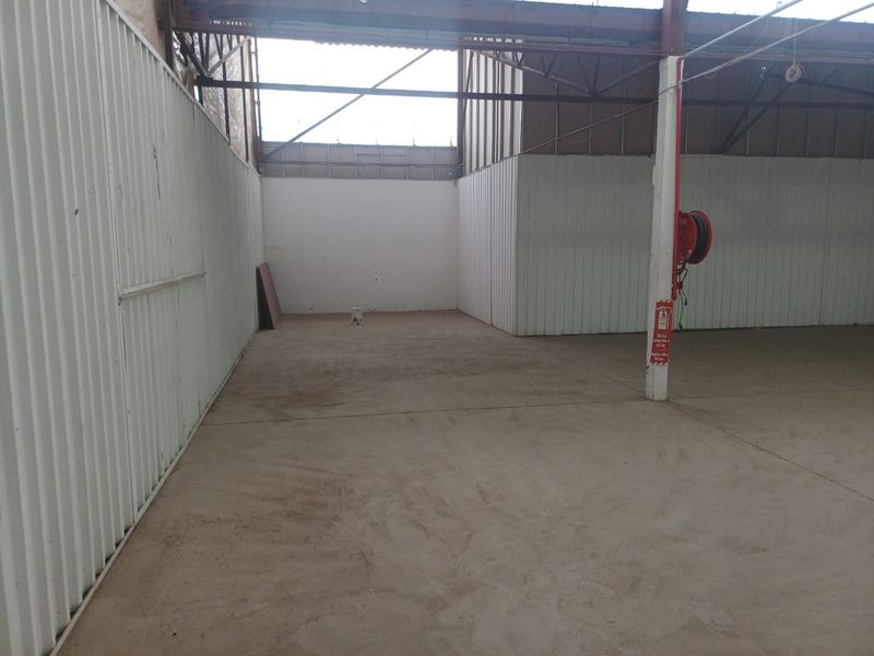 An open-plan industrial utility space featuring corrugated metal walls, exposed steel roof trusses, and concrete flooring, equipped with a wall-mounted fire hose reel.
