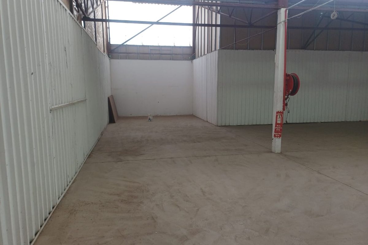An open-plan industrial utility space featuring corrugated metal walls, exposed steel roof trusses, and concrete flooring, equipped with a wall-mounted fire hose reel.