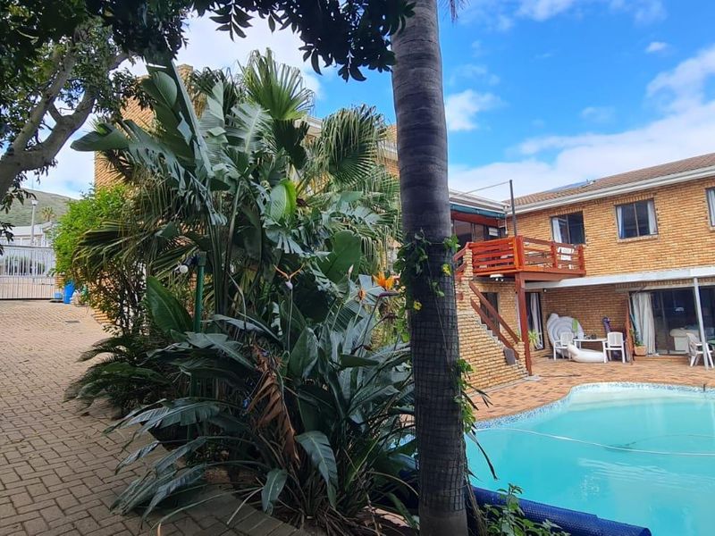Rear exterior view of the property featuring a swimming pool, brick paved courtyard, and an elevated wooden deck with external staircase access.