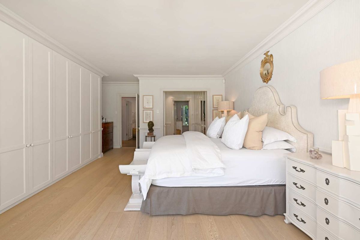 Spacious bedroom featuring extensive floor-to-ceiling built-in cabinetry, light timber flooring, and elegant crown molding throughout.