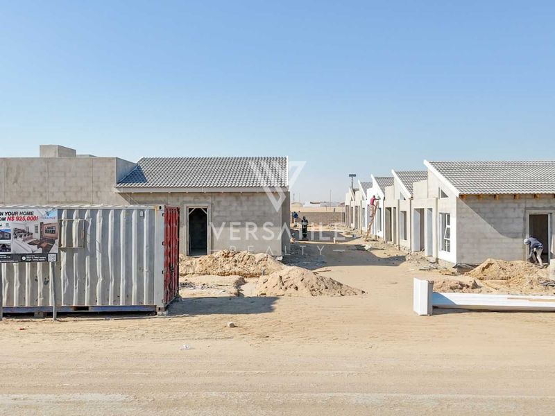 A construction site showing a row of townhouse units in the early stages of development with unfinished exterior walls and roofing.