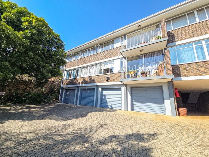 Exterior view of a multi-story apartment building featuring brick facade, private balconies, and ground-level garage access with a paved driveway.