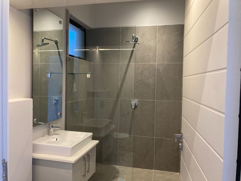 Modern bathroom featuring a sleek vanity with ceramic basin, large wall mirror, and a spacious walk-in shower with grey tiled finishes.