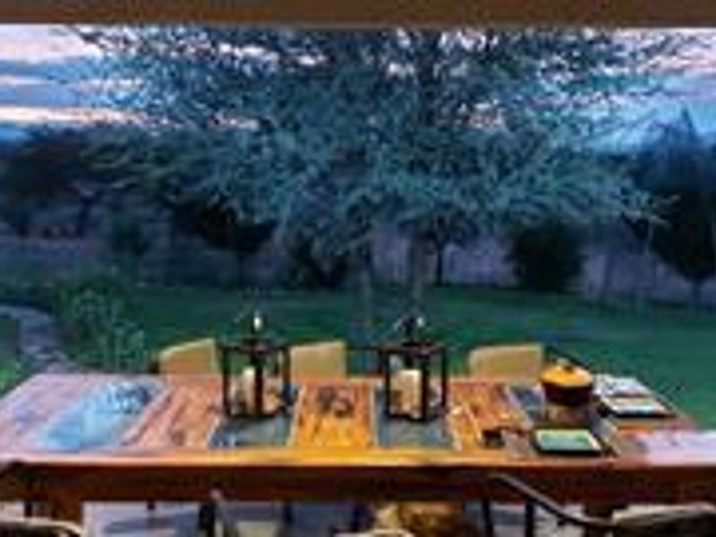 A spacious covered patio area featuring tiled flooring and structural pillars, offering an open view of the garden and surrounding landscape.