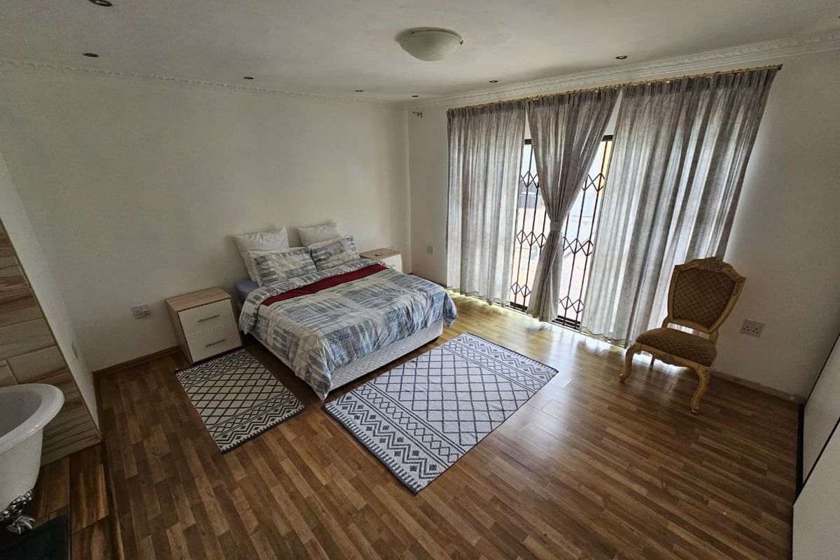 Spacious bedroom featuring wood-look laminate flooring, recessed ceiling lighting, and a sliding door with security gate leading to an outdoor area.