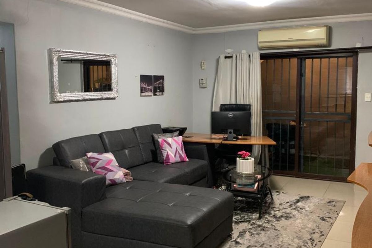 A living room featuring tiled flooring, crown molding, and a sliding glass door with security gate leading to an outdoor area.