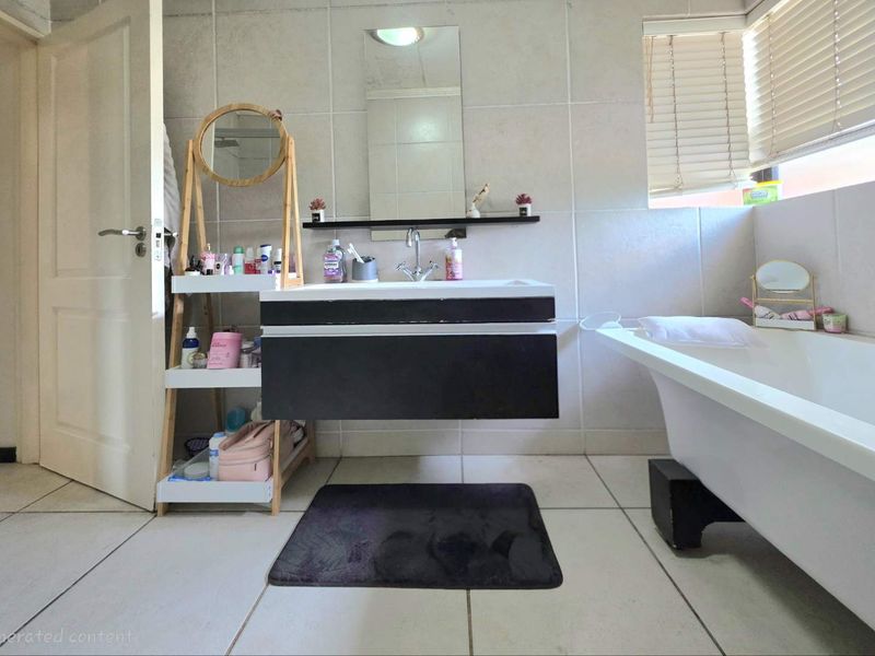 Bathroom featuring a wall-mounted vanity, freestanding bathtub, and neutral wall tiling with natural light provided by a window with venetian blinds.