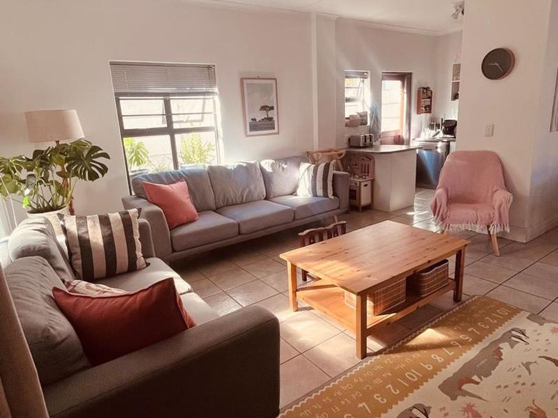 An open-plan living area featuring tiled flooring, a ceiling fan, and a connected kitchen space with neutral wall finishes.