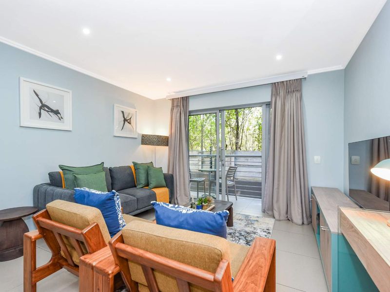 A well-lit living room featuring tiled flooring, recessed downlights, and a sliding glass door providing access to an outdoor balcony area.