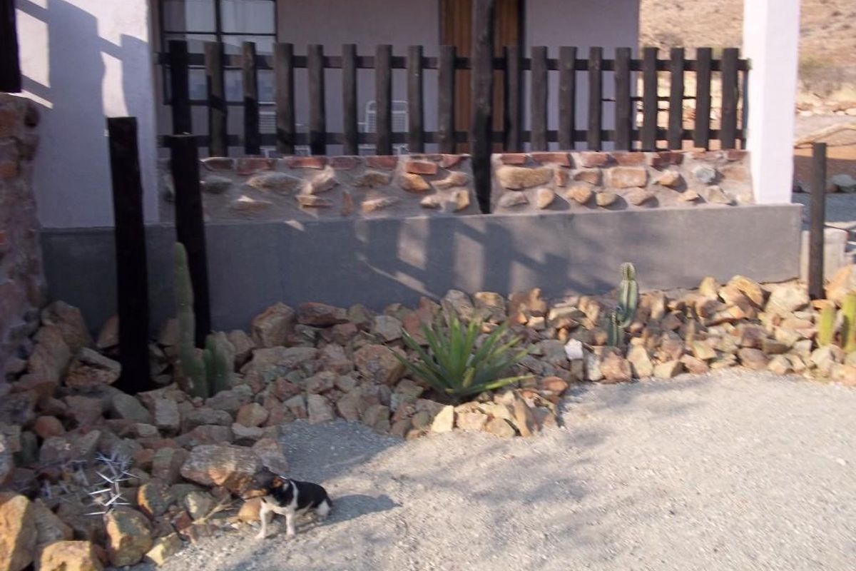 Exterior view of a farm property featuring a stone-walled patio area with a wooden fence and landscaped rock garden.