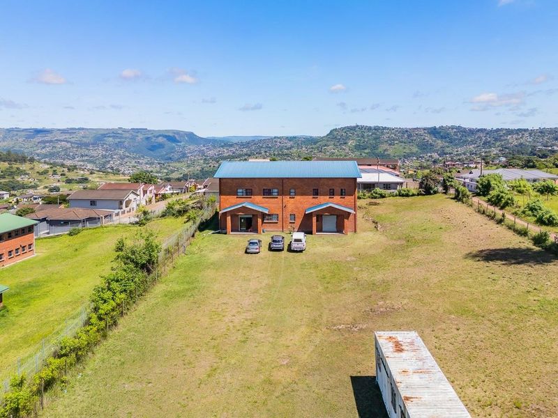 Aerial view of a large residential vacant land plot featuring a double-story brick building with a metal roof and perimeter fencing.