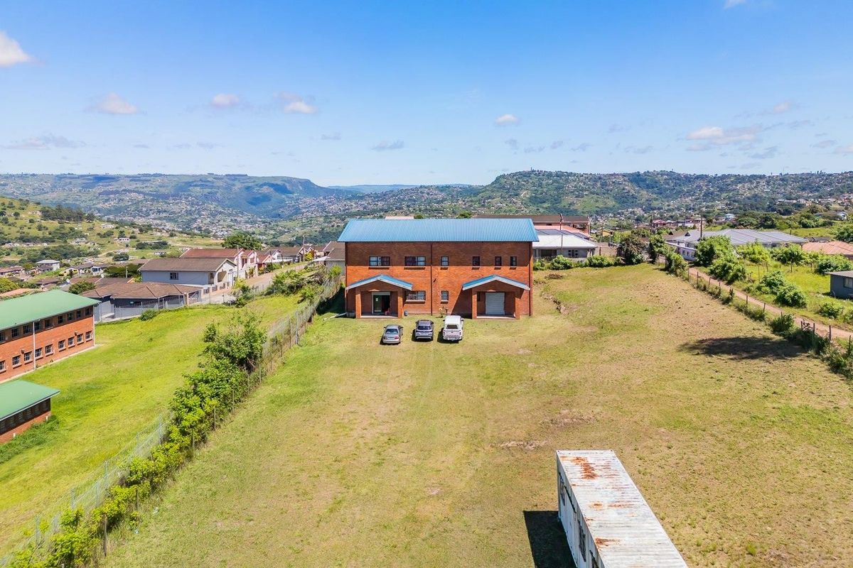 Aerial view of a large residential vacant land plot featuring a double-story brick building with a metal roof and perimeter fencing.
