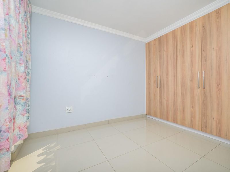 A clean, empty bedroom featuring light-colored tiled flooring and modern wood-finish built-in cupboards with ample storage space.