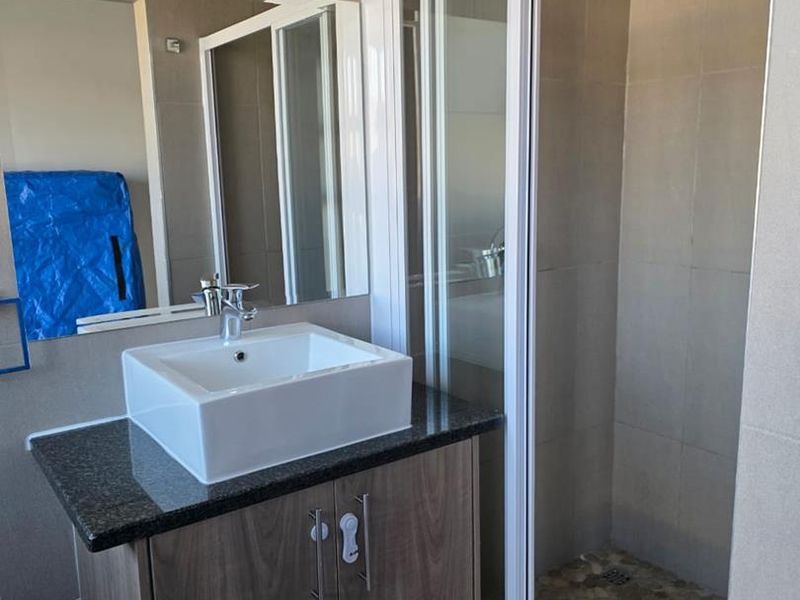 Modern bathroom featuring a vanity with a vessel sink, granite countertop, and a walk-in shower with a rain shower head and pebble tile flooring.