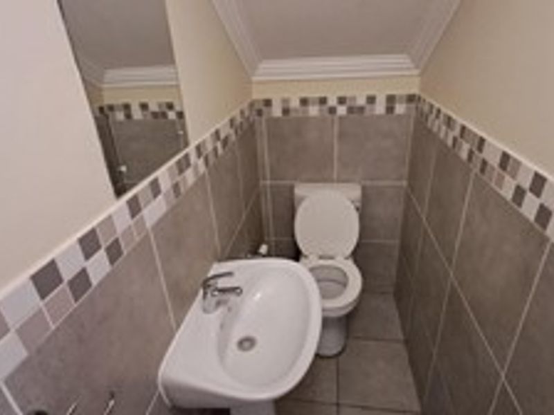 A compact guest bathroom featuring a pedestal washbasin, toilet, and neutral-toned tiled walls with a decorative mosaic border.