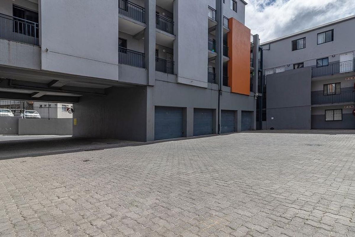 Exterior view of the apartment complex featuring a paved parking area, multiple garage doors, and multi-story residential building facade.