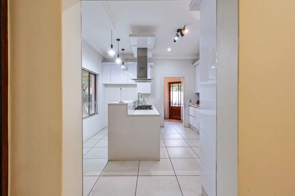 Modern kitchen featuring white cabinetry, a central island with a built-in gas hob, stainless steel extractor fan, and tiled flooring.