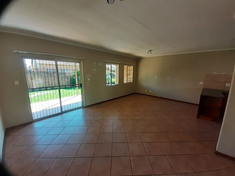 Spacious open-plan living area featuring tiled flooring, large windows, and a sliding door leading to the exterior, with an adjacent kitchen corner.