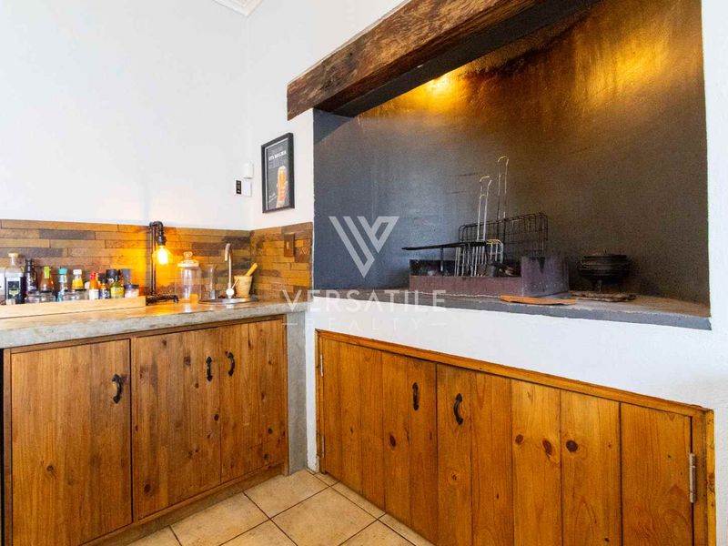 Indoor entertainment area featuring a built-in braai, rustic timber cabinetry, concrete countertops, and a prominent exposed timber beam.