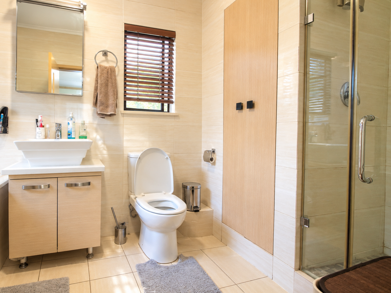 A well-maintained bathroom featuring a modern vessel sink vanity, a glass-enclosed shower, and neutral wall tiling with natural light from a window.