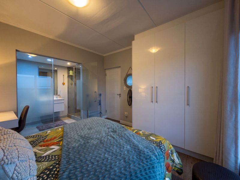 Modern bedroom featuring built-in cupboards and an integrated en-suite bathroom with a glass-enclosed shower and vanity.