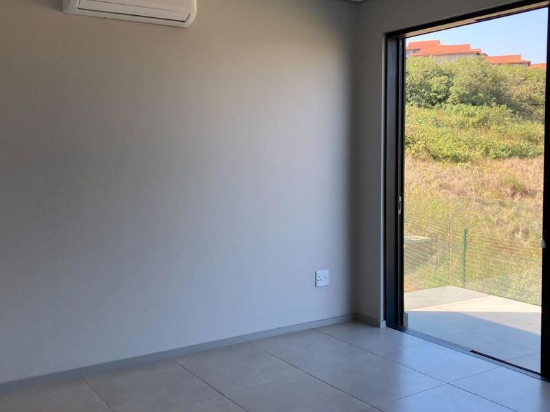 A bright, empty bedroom featuring tiled flooring, a wall-mounted air conditioning unit, and large sliding glass doors opening to an outdoor area.