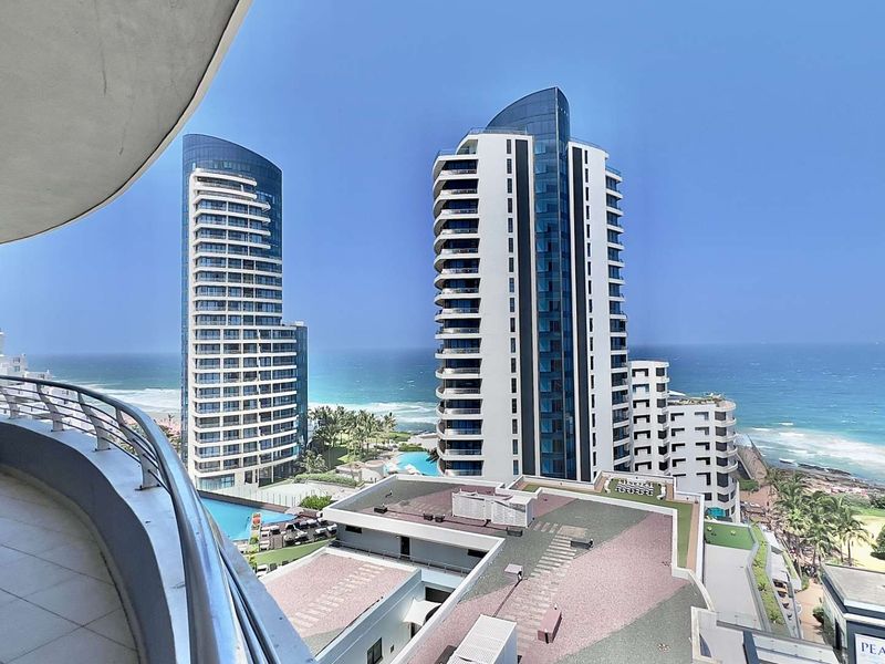 A spacious curved balcony featuring tiled flooring and a stainless steel balustrade, offering expansive views of the ocean and surrounding high-rise buildings.