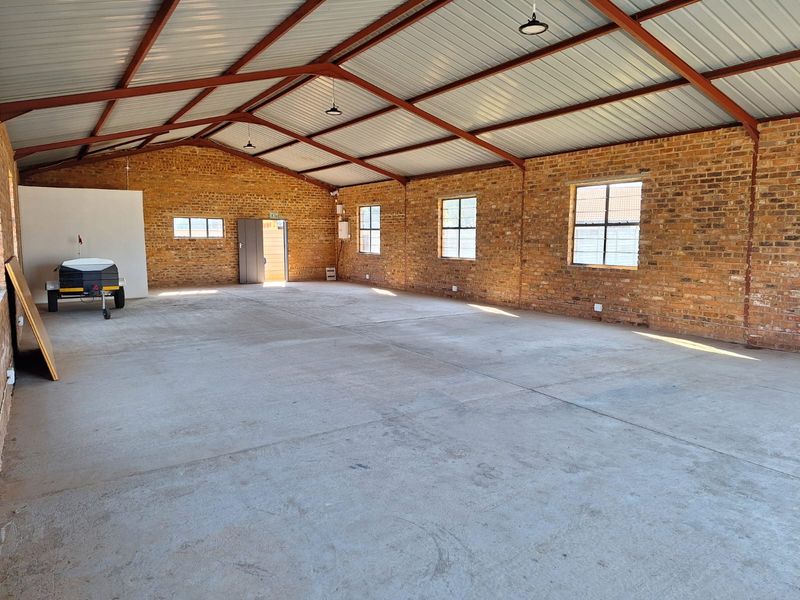 Spacious industrial utility area featuring exposed brick walls, concrete flooring, and high-clearance steel roof trusses, suitable for various commercial or storage applications.