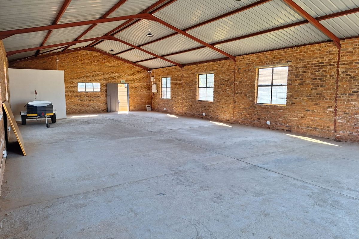 Spacious industrial utility area featuring exposed brick walls, concrete flooring, and high-clearance steel roof trusses, suitable for various commercial or storage applications.