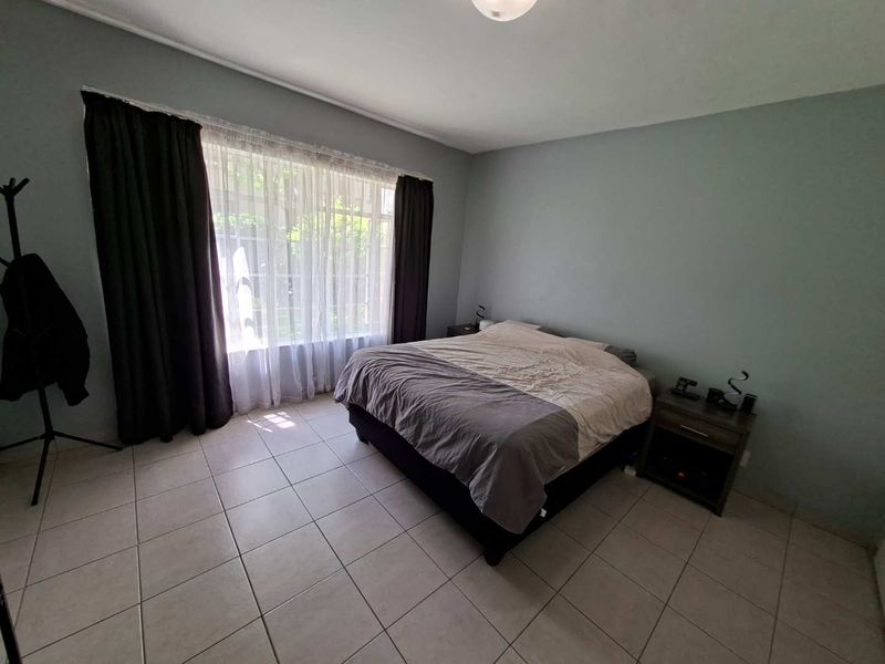 A spacious bedroom featuring neutral tiled flooring and a large window that allows for ample natural light.
