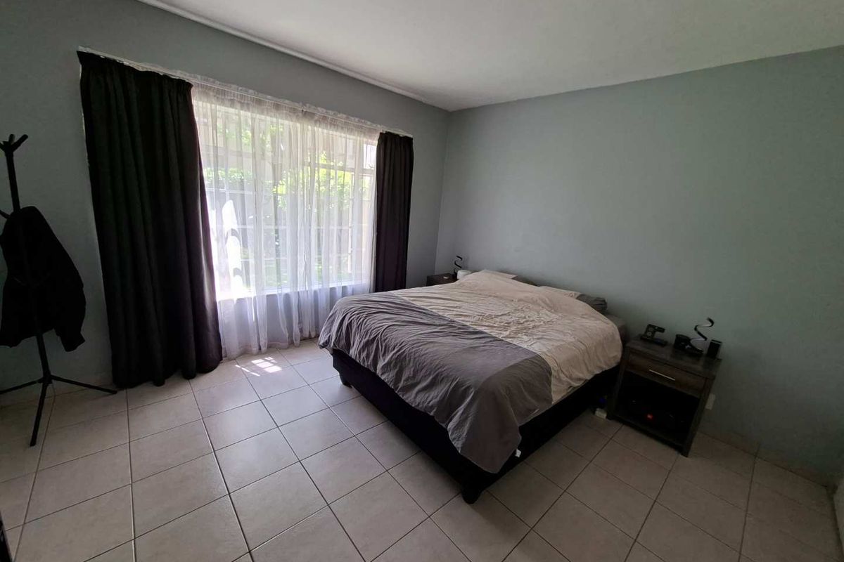 A spacious bedroom featuring neutral tiled flooring and a large window that allows for ample natural light.