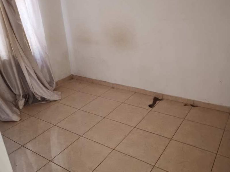 An empty bedroom featuring tiled flooring and plain walls, requiring minor repairs and cosmetic updates.