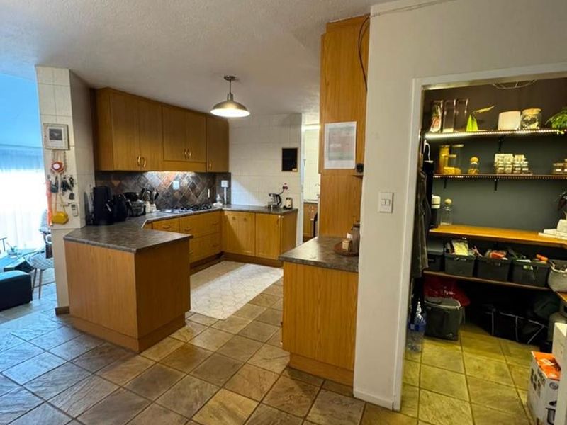 Open plan kitchen featuring wooden cabinetry, laminate countertops, and tiled flooring, with an adjacent walk-in pantry area.