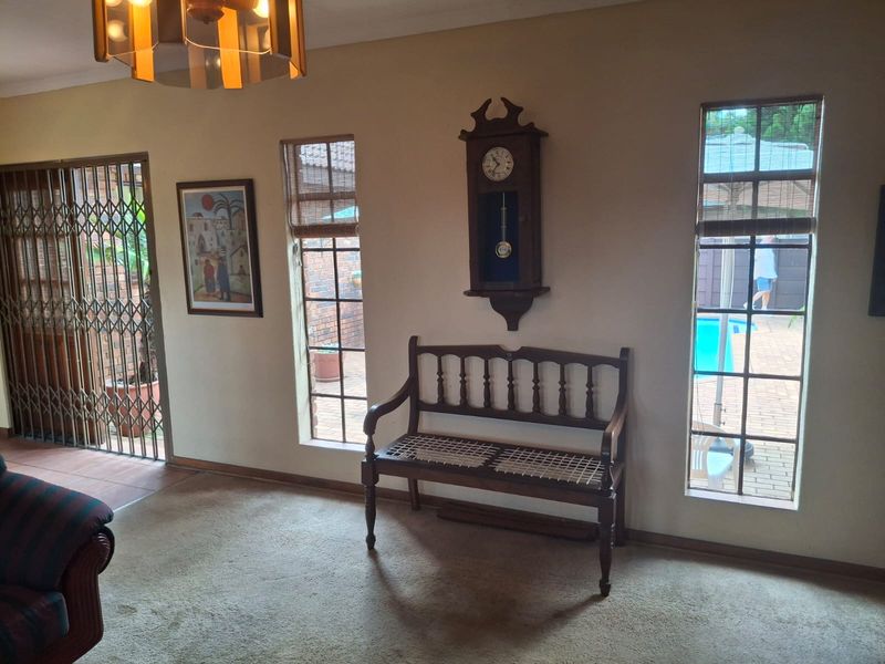 A living room area featuring carpet flooring, security gates, and large windows providing a view of the outdoor pool area.