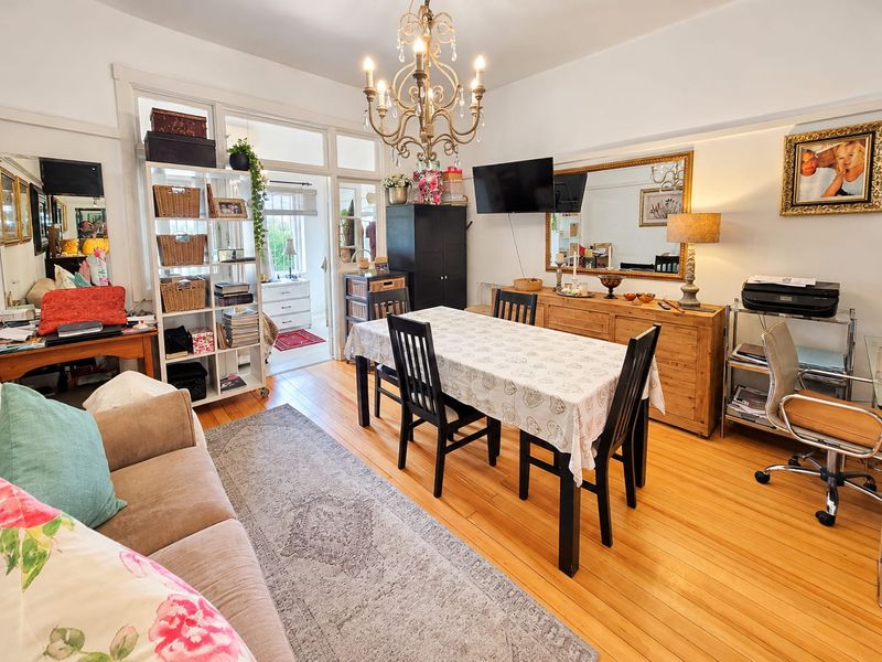 A bright living and dining area featuring polished hardwood flooring, a classic chandelier, and elegant french doors leading to an adjacent room.