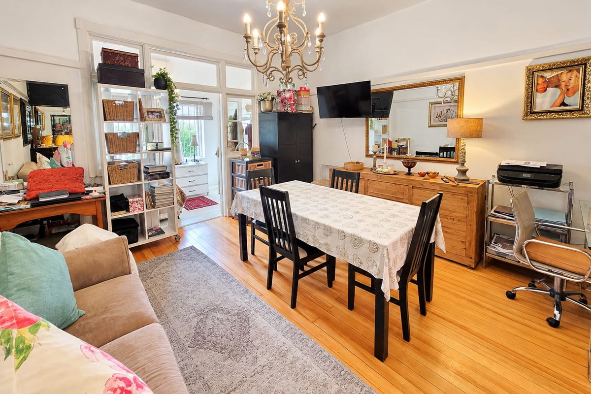 A bright living and dining area featuring polished hardwood flooring, a classic chandelier, and elegant french doors leading to an adjacent room.