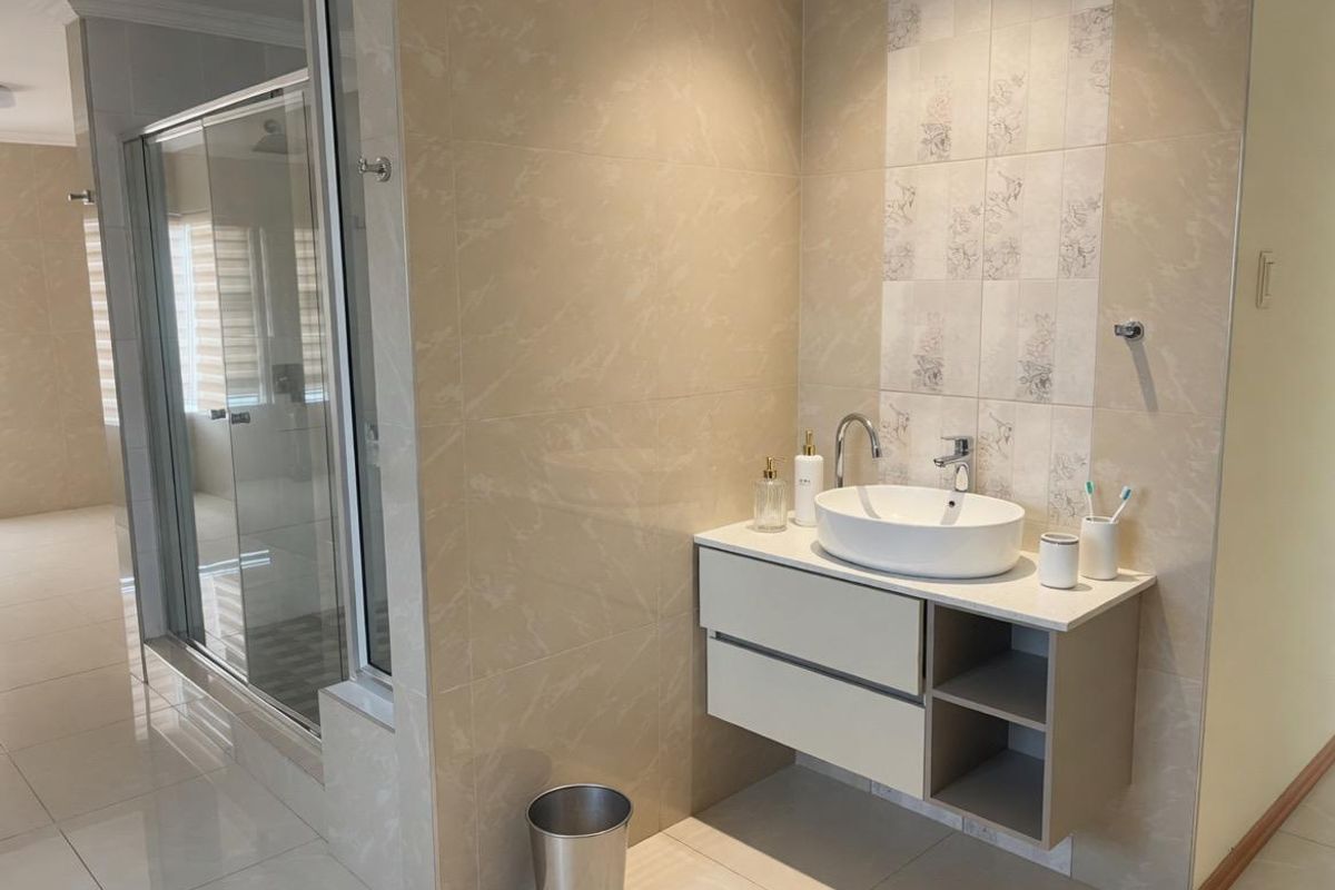 Modern bathroom featuring a floating vanity with a vessel sink, large format wall tiles, and a glass-enclosed shower area.