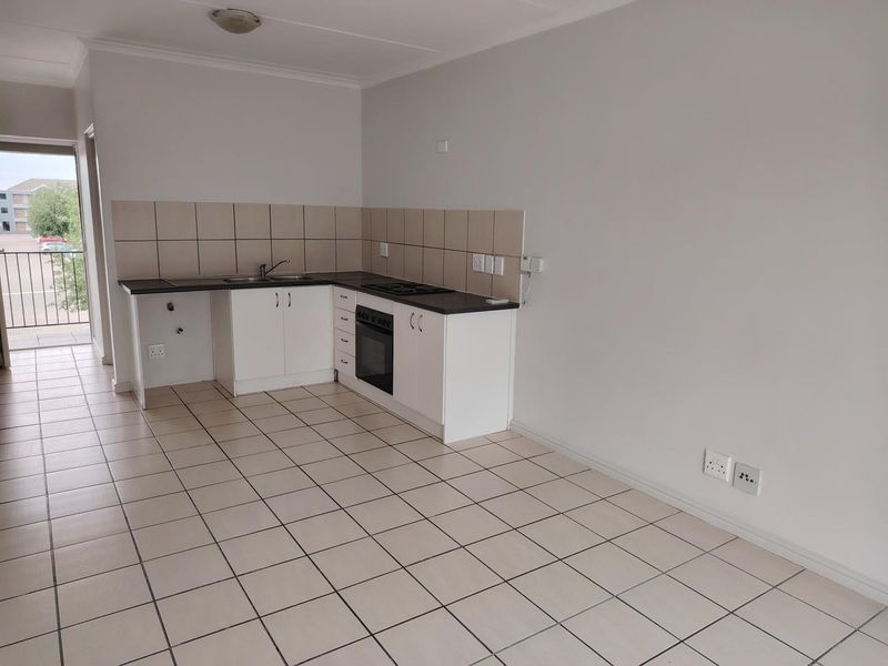 Open-plan kitchen area featuring white cabinetry, dark countertops, built-in oven and hob, tiled splashback, and ceramic floor tiles, leading to a balcony.