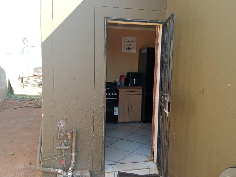 Exterior view of a rear entrance featuring a security gate, external plumbing fixtures, and a concrete base area.