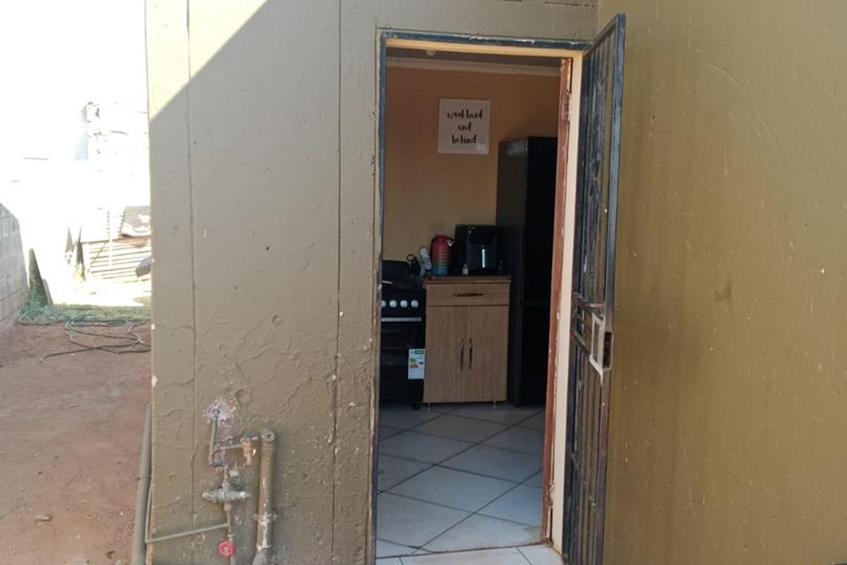 Exterior view of a rear entrance featuring a security gate, external plumbing fixtures, and a concrete base area.